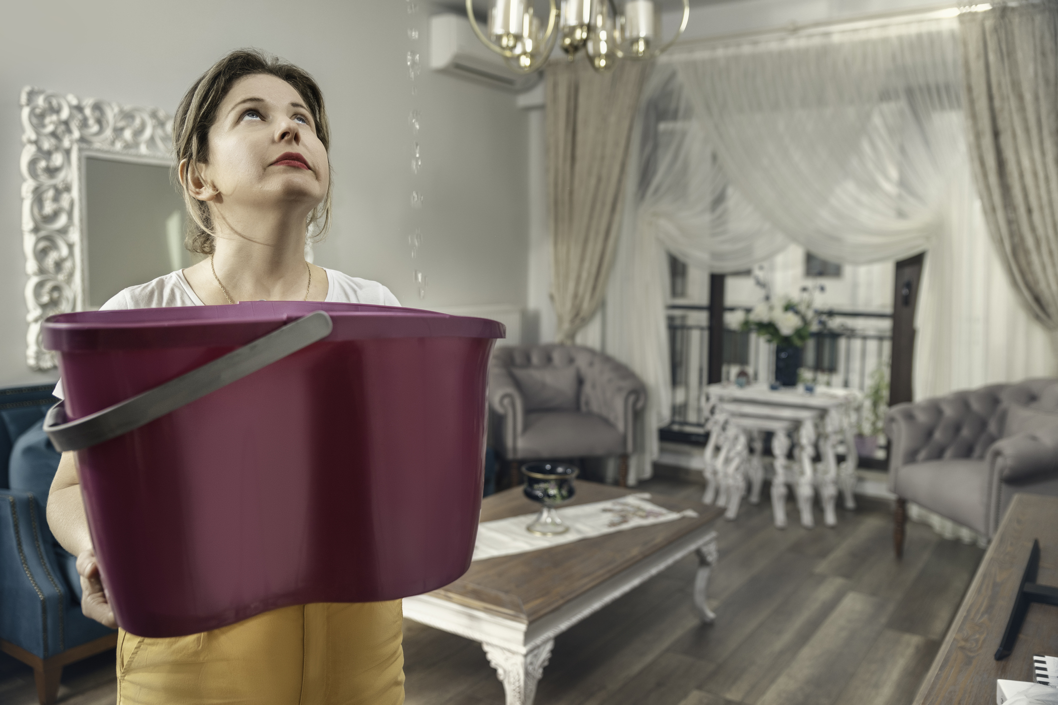 House Ceiling is Flowing - Woman Holding Bucket While Water Droplets Leak From Ceiling